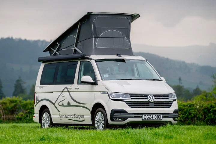 White VW pop-top camper van for RV rental, with mountain decals, parked in a grassy field.. Volkswagen California Ocean 2024