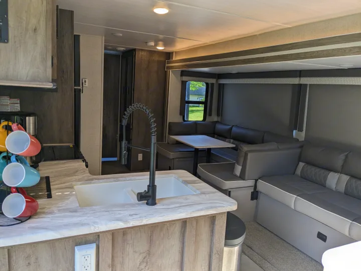 Spacious RV rental interior: modern kitchen with sink and vibrant mugs, alongside a comfy U-shaped dinette.. Forest River Wildwood 2021