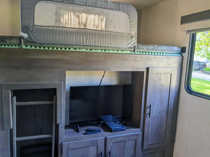 RV rental interior featuring a cozy bunk bed with a safety rail, an entertainment center with TV, and storage.. Forest River Wildwood 2021