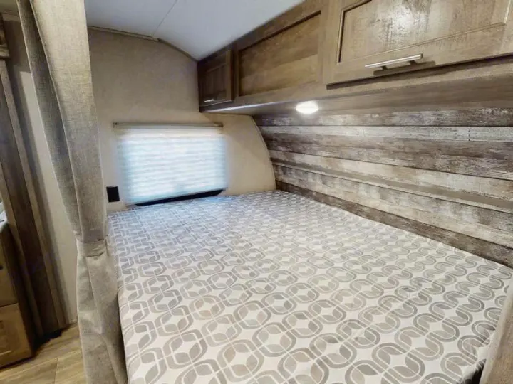 RV rental bedroom: comfortable bed with modern pattern, wood-paneled wall, overhead cabinets, and window blind.. Forest River Xlr Thunrderbolt 2022