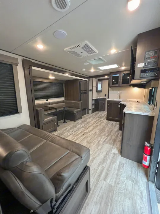 RV rental interior: Spacious living area with a dark sofa, dinette, kitchen, and light wood-look flooring.. Grand Design Transcend Xplor 265BH 2021