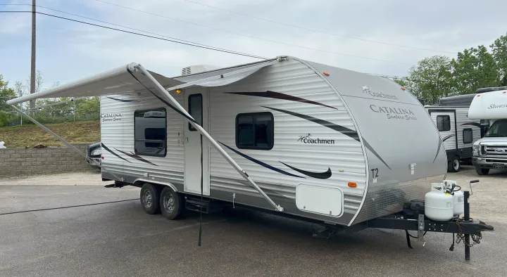 Light grey travel trailer RV with extended awning on display for rental. Two propane tanks visible upfront.. Coachmen Catalina 2012