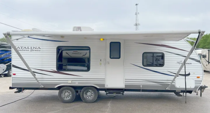 A white Coachmen Catalina travel trailer with an extended awning, parked on asphalt. Perfect for your next rv rental getaway.. Coachmen Catalina 2012