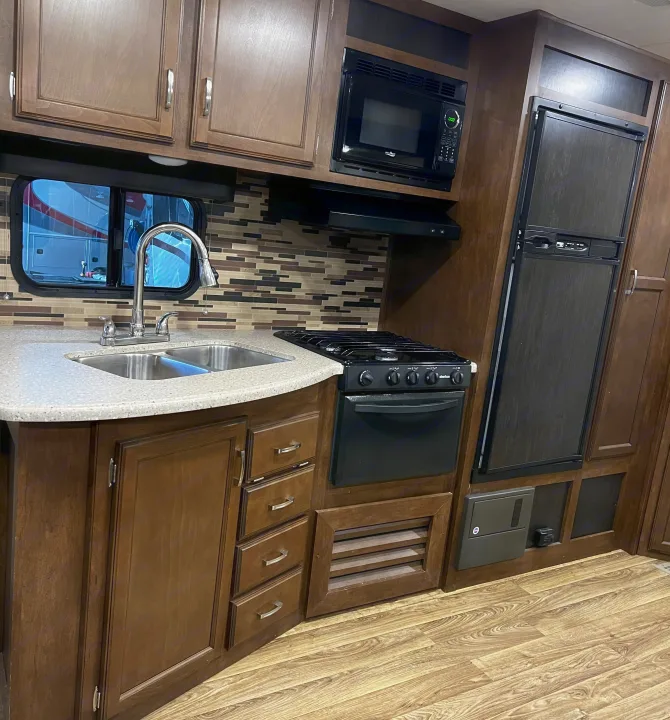 Modern RV rental kitchen interior with wood cabinets, light counters, sink, microwave, stove, & fridge.. Venture Sport Trek 2017