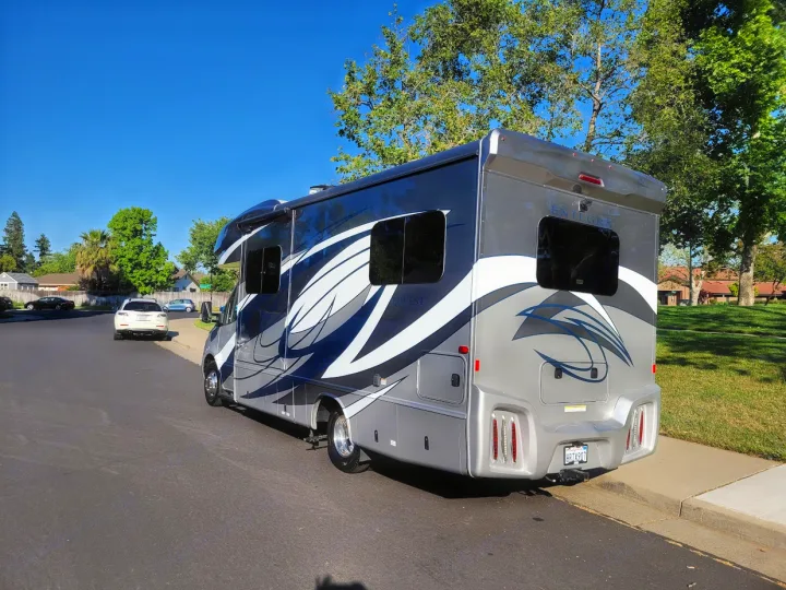 A sleek gray and white rv rental, featuring graphic decals, parked on a sunny residential street.. Entegra Coach Qwest 2020