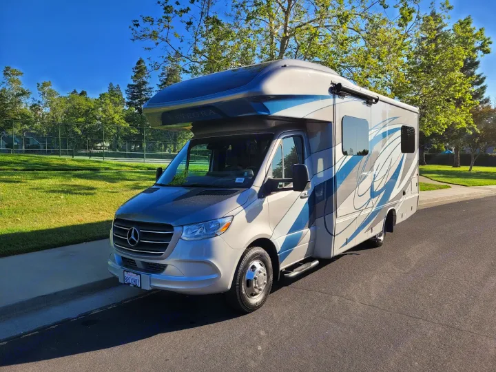 This silver and blue Entegra RV rental, built on a Mercedes-Benz chassis, is parked near a tennis court.. Entegra Coach Qwest 2020