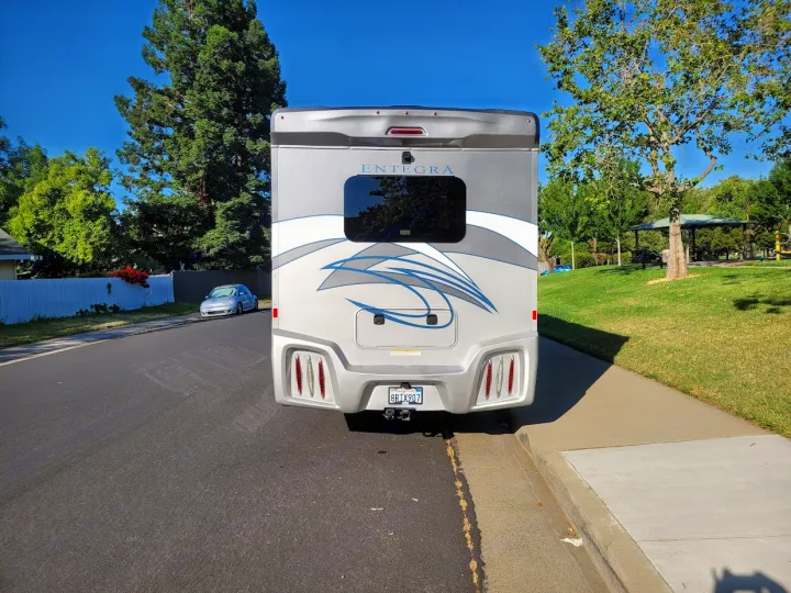 Rear view of a large silver Entegra RV parked roadside on a sunny day. Ideal for an RV rental getaway.. Entegra Coach Qwest 2020