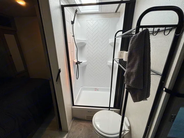 RV rental bathroom features: modern shower, toilet, and shelving with towels, hinting at an adjacent sleeping area.. Forest River 296 QBLE 2023