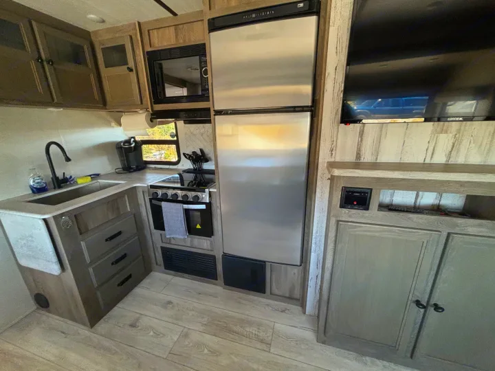 RV rental kitchen: modern interior with stainless steel fridge, microwave, stove, sink, and flat-screen TV.. Forest River 296 QBLE 2023