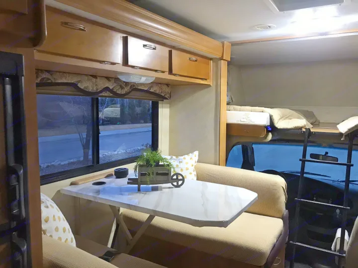 Interior of a cozy RV rental, featuring a dining area, overhead cabinets, and an inviting bunk bed with ladder access.. Forest River Sunseeker 2008