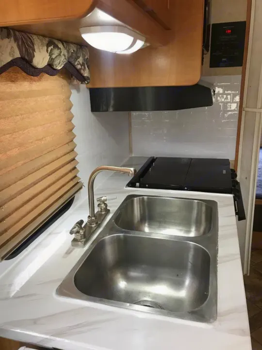 This RV rental features a bright, updated kitchen with double sink, stove, white countertop, and tiled backsplash.. Forest River Sunseeker 2008