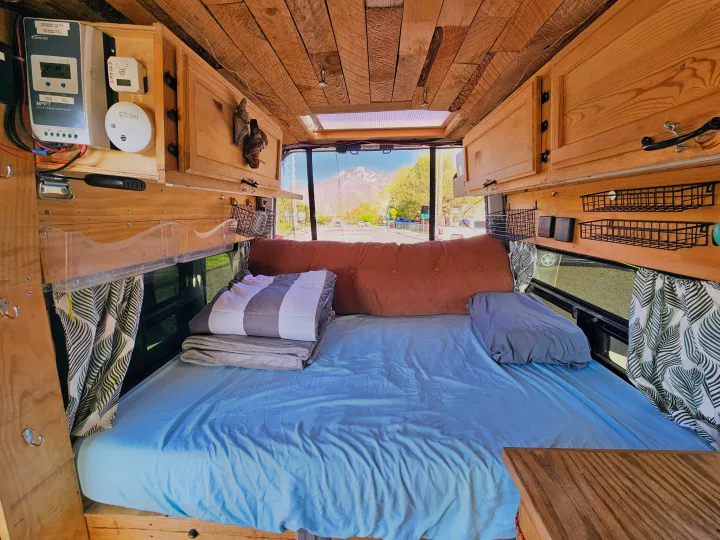 RV rental: Inside a custom camper, admire the cozy bed, wooden ceiling, solar setup, and mountain view outside.. Nissan Other 2012