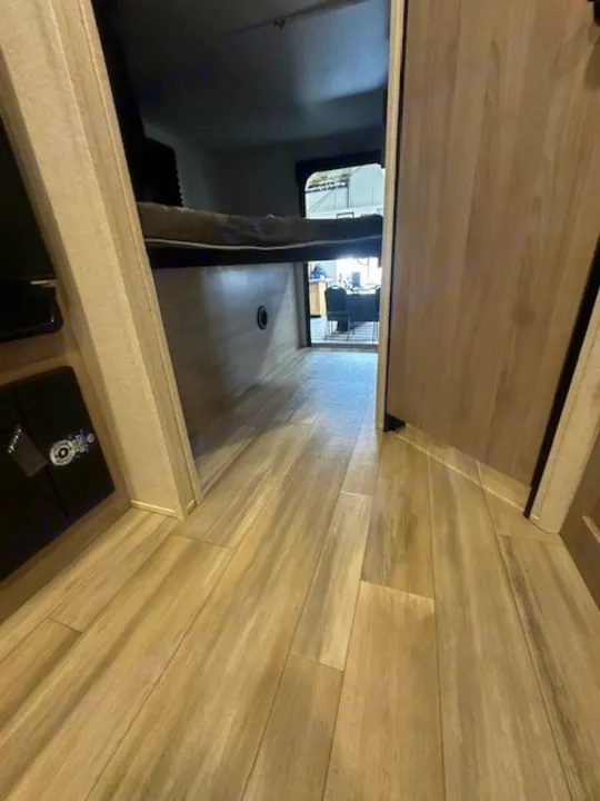 RV rental interior: light wood flooring and raised bed leading to a bright room at the end.. Coachmen 2146BHX 2023