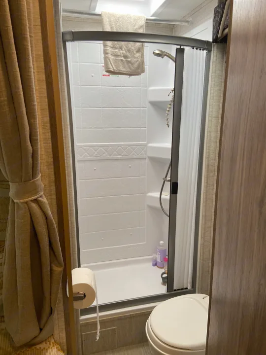 Inside an RV rental, this compact bathroom features a white shower stall, toiletries, a towel, and a toilet with toilet paper.. Jayco Redhawk SE 2021