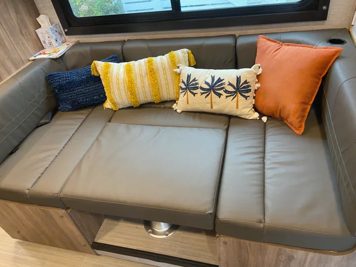 Inside an RV rental: L-shaped dinette couch with colorful pillows and window view, offering a cozy living space.. Jayco Redhawk SE 2021