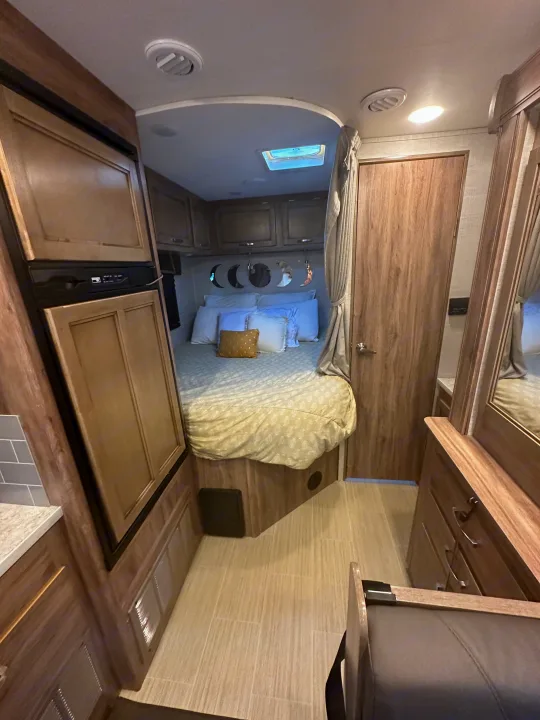 Step inside this RV rental, featuring a cozy bedroom with moon decor, a compact kitchen with a fridge, and efficient storage.. Jayco Redhawk SE 2021