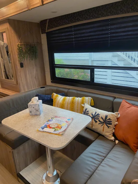 Cozy RV rental dining area with a table, plush seating, colorful pillows, and a window revealing a rainy outdoor view.. Jayco Redhawk SE 2021