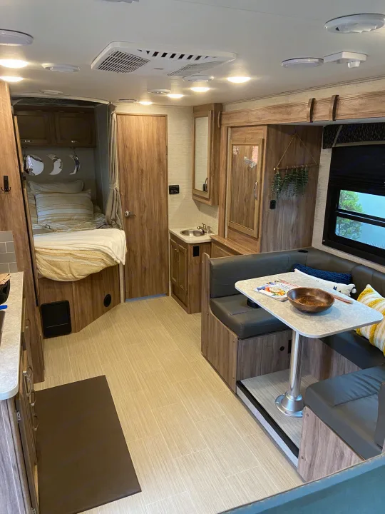 Inside a clean RV rental: modern design with a bed, vanity sink, and dining booth. Features light wood tones.. Jayco Redhawk SE 2021