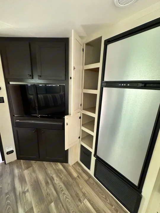RV rental interior: A compact living/kitchenette area featuring a TV, dark cabinets, pantry, and stainless steel refrigerator.. Highland Ridge RV Open Range 2022
