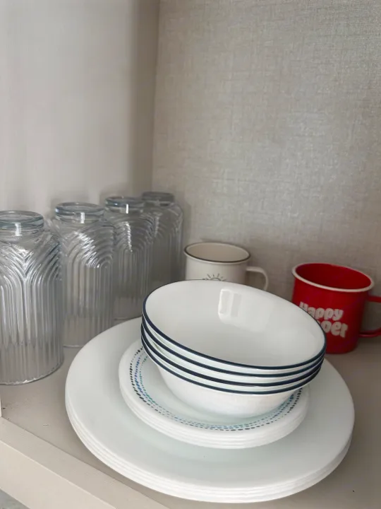 Compact kitchen setup in an RV rental: stacks of white plates, bowls, glass jars, and enamel mugs neatly arranged.. Highland Ridge RV Open Range 2022