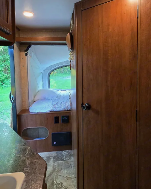 This RV rental interior features a comfortable sleeping bunk, a window with a serene forest view, and warm wood cabinetry.. Jayco Jay Feather 7 XRB 2016