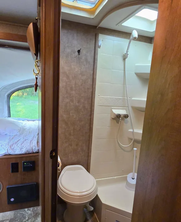 RV rental interior: compact bathroom with toilet and shower, plus a peek into the sleeping area with outdoor view.. Jayco Jay Feather 7 XRB 2016