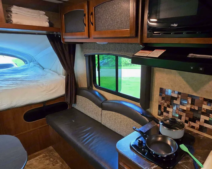 Inside an RV rental, showing a bed, comfortable seating area, and compact kitchen with cooking essentials.. Jayco Jay Feather 7 XRB 2016