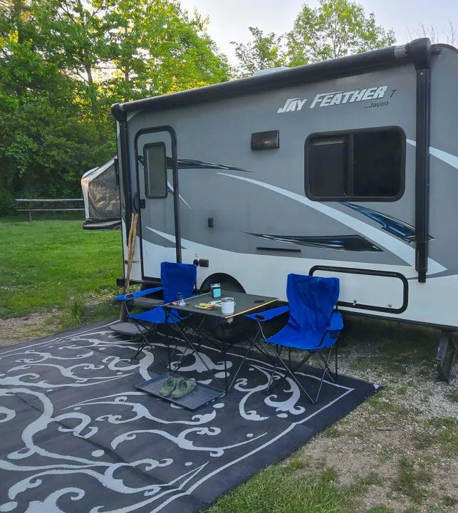 RV rental ready for relaxation. A grey travel trailer with a cozy outdoor setup: blue chairs, table, and patterned rug.. Jayco Jay Feather 7 XRB 2016