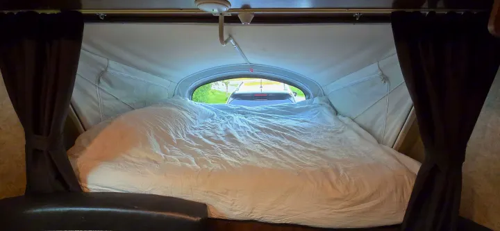 Cozy RV rental interior: large bed, tied-back curtains, and window view looking out of the pop-up camper.. Jayco Jay Feather 7 XRB 2016