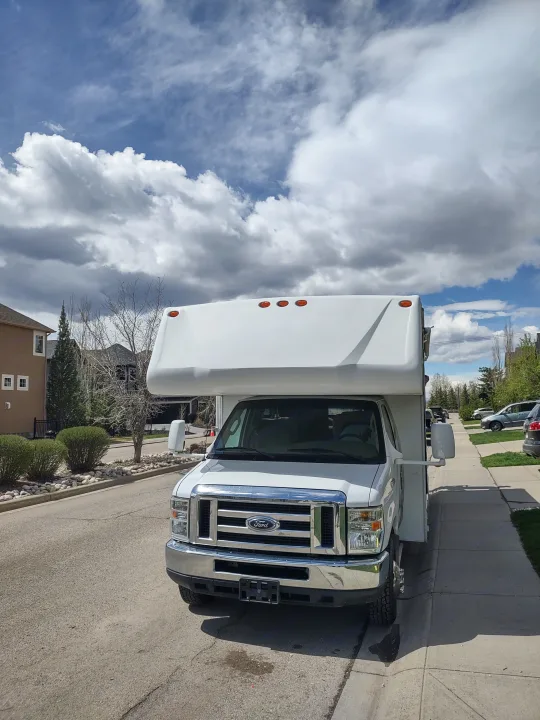 Bright white RV rental parked on a residential street. A Class C RV under a partly cloudy sky, with houses & trees visible.. Forest River Sunseeker 2008