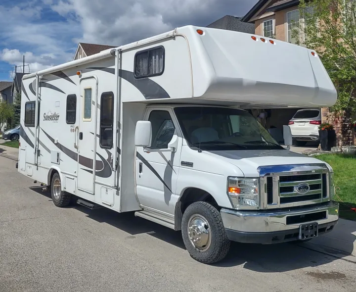 White Ford "Sunseeker" Class C rv rental with black/gray decals, parked on a sunny street near homes.. Forest River Sunseeker 2008