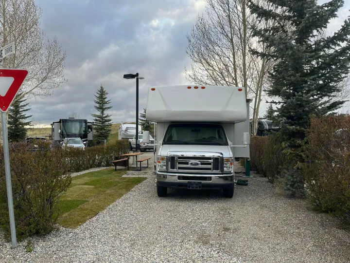 White rv rental parked on a gravel site in a busy campground under an overcast sky, with trees and other RVs.. Forest River Sunseeker 2008