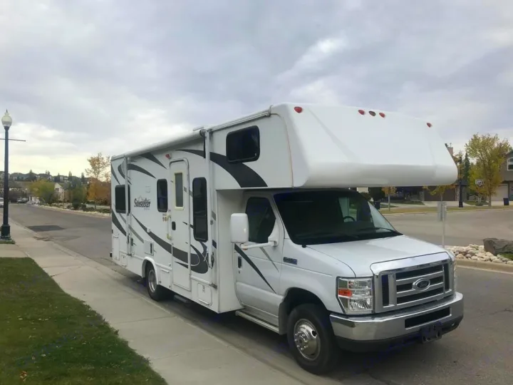 White Sunseeker Class C RV rental, with bold graphics, parked on a residential street.. Forest River Sunseeker 2008