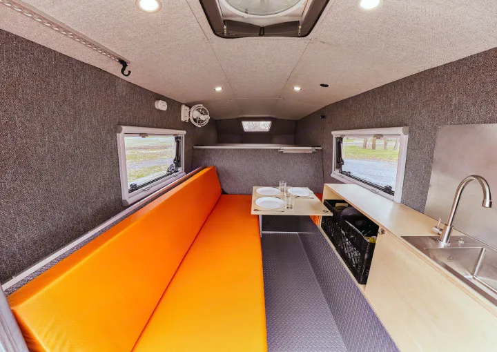 Bright interior of an RV rental: a long orange bench, a compact table, and a built-in kitchenette with a sink.. Gmc sierra 1500 2024