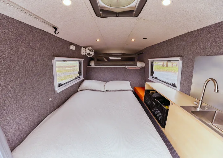 RV rental interior featuring a large bed, compact kitchen with sink, and overhead bunk. Ideal for camper adventures.. Gmc sierra 1500 2024