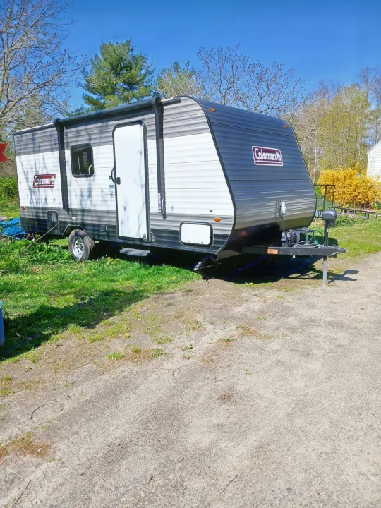Coleman travel trailer, an ideal RV rental, parked on gravel in a sunny outdoor setting. Ready for camping adventures!. Coleman Lantern 2021