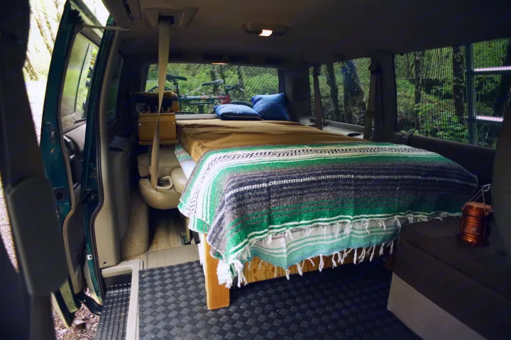 Cozy camper van interior: bed, pillows, bike, forest view. Perfect for RV rental adventures.. Chevrolet Astro Van AWD 1998