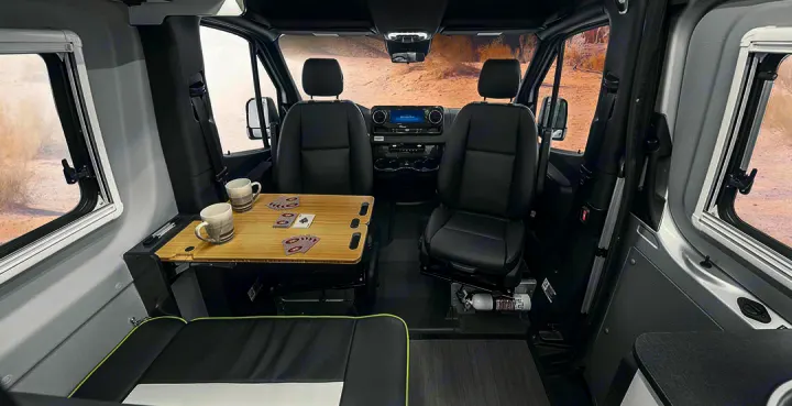 Inside an RV rental, showing swivel seats, a table for games/dining, and a compact, functional living area.. Winnebago Revel 2020