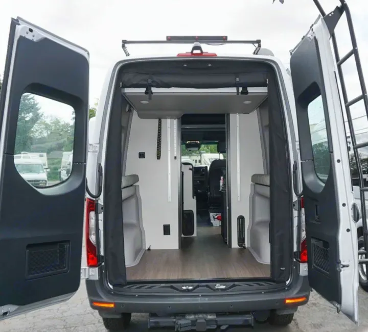 Spacious RV rental van: rear view with open doors revealing modern interior, bed platform, wood floor, & ladder on right.. Winnebago Revel 2020
