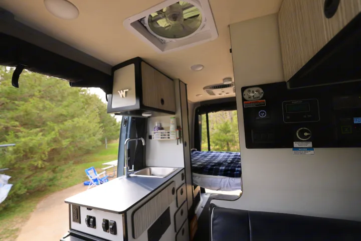 Spacious RV rental interior with kitchenette, solar controls, and a cozy bed, ready for outdoor adventures.. Mercedes Winnebago Revel 2023