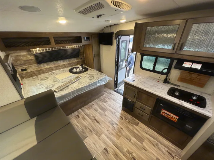 Explore this efficient RV rental interior, featuring a modern kitchen, a bed, and a cozy living area with wood-look floors.. Sonic Lite 2022