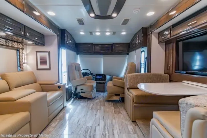 Spacious, luxurious RV rental interior. Features front cockpit, tan sofa, dining booth, TV, and wood-look flooring.. Entegra Coach Reatta 2022
