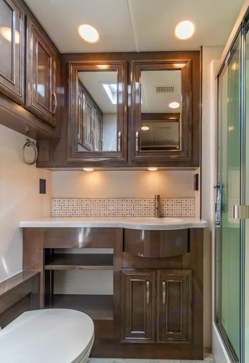 Modern RV rental bathroom features a vanity, integrated sink, mirrored cabinets, toilet, and shower. Bright lighting.. Entegra Coach Reatta 2022