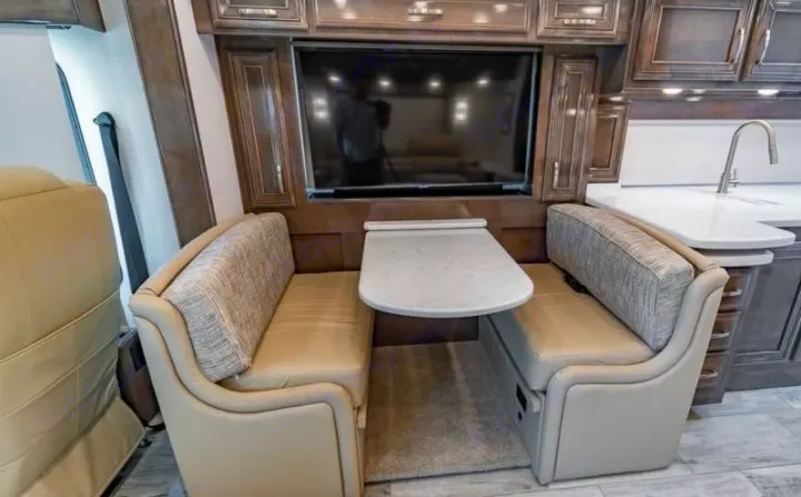 RV rental interior: cozy dinette with opposing benches, table, TV, and an adjacent kitchen with sink.. Entegra Coach Reatta 2022