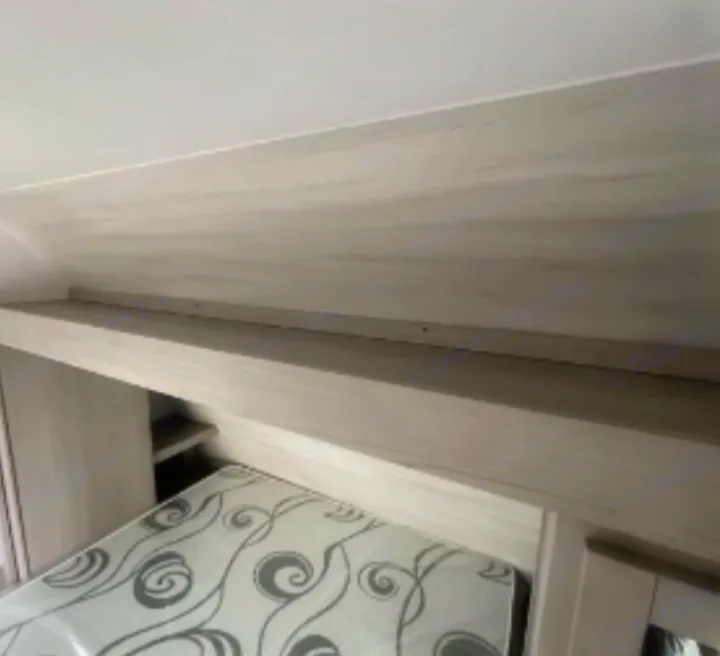 Light-toned RV rental bedroom with patterned mattress under integrated overhead shelf.. Dutchmen Kodiak SE 2023