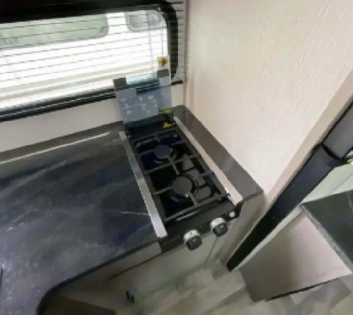 Compact RV rental kitchen: two-burner stove, dark countertop, and window. Ideal for mobile cooking.. Dutchmen Kodiak SE 2023