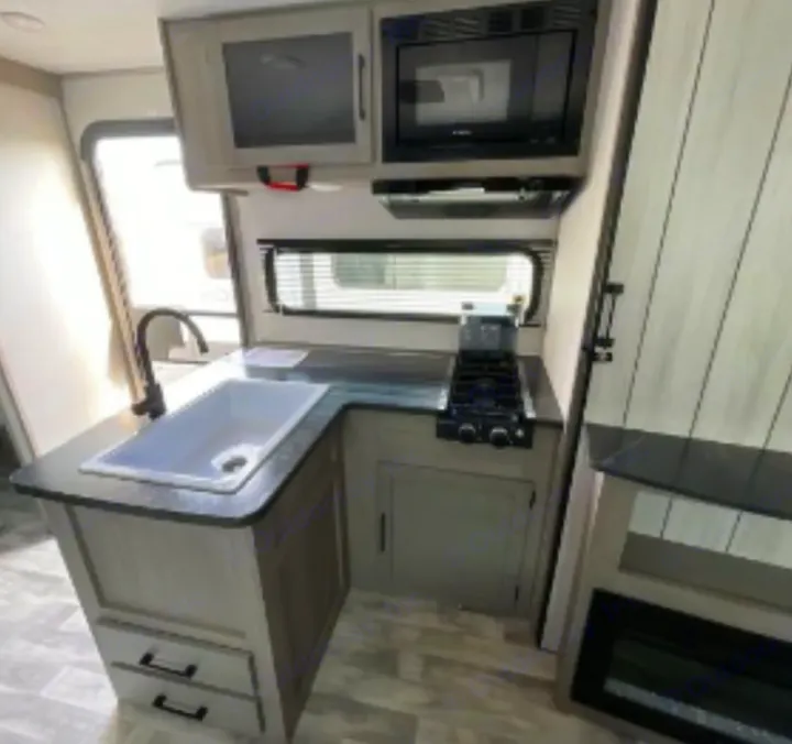 Modern RV rental kitchen with sink, stovetop, microwave, and cabinets. Perfect for your next travel adventure.. Dutchmen Kodiak SE 2023