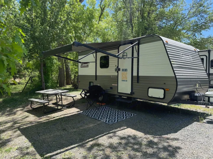 Coleman RV rental set up at a shaded campsite, featuring an extended awning, picnic table, and outdoor area.. Dutchmen Coleman Lantern LT 2023
