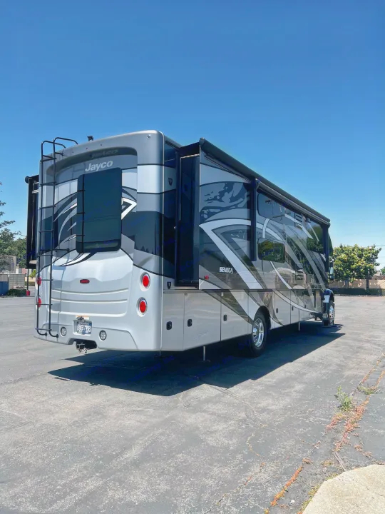 A large, modern grey and black Jayco Seneca motorhome, ideal for rv rental, is parked on asphalt under a clear blue sky.. Jayco Seneca 2021