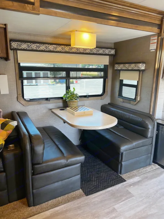 Cozy RV rental dinette interior featuring black seating, a table, and windows, ideal for travel.. Jayco Seneca 2021